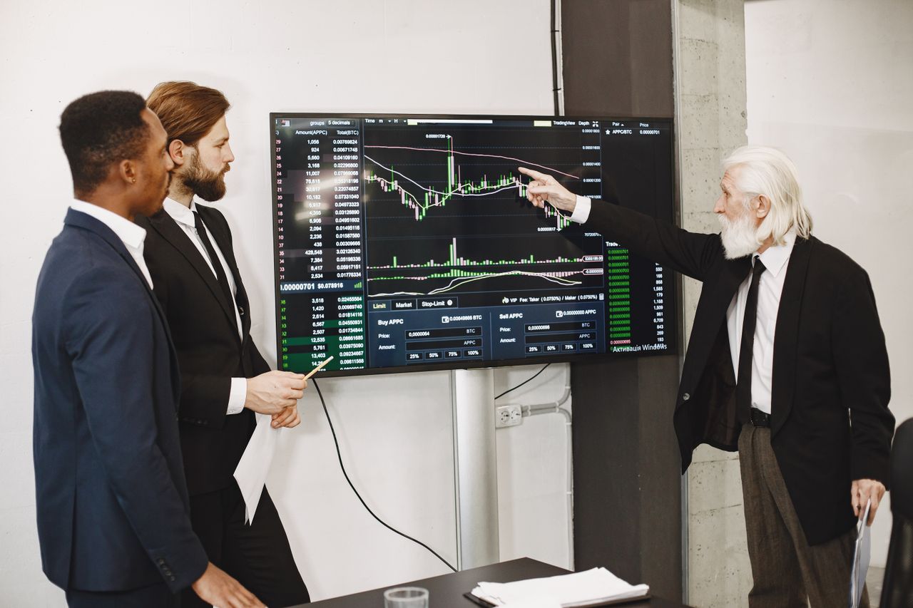 gallery-4 A diverse business team in a meeting analyzing stock market data on a screen.