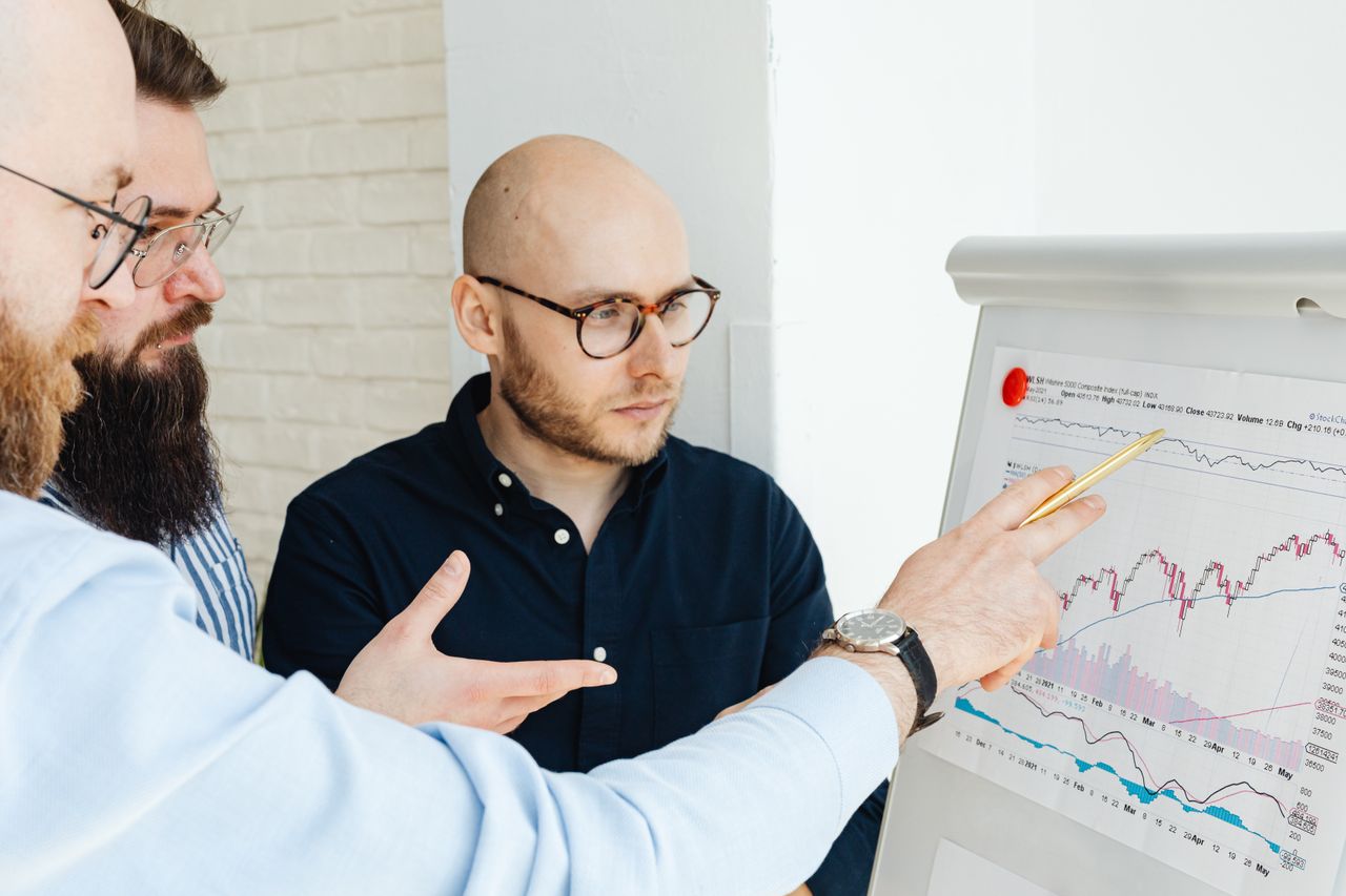services-03 Three men discussing financial charts on a whiteboard during a business meeting.